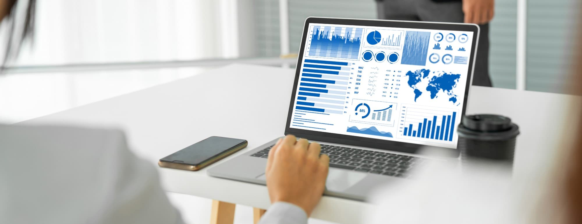 Two laptop screens side by side on a desk showing a website analytics dashboard with a session funnel and a CRM contact record, soft window light from the left