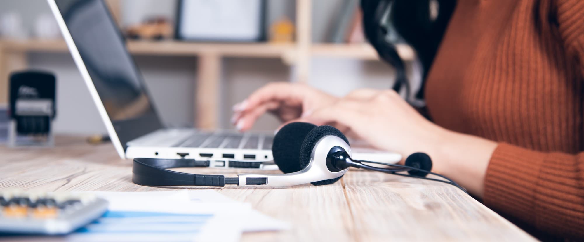 A customer support agent's empty headset resting on a desk beside a glowing monitor at dusk, suggesting the handover between a chatbot and a human that decides whether the ROI case lands