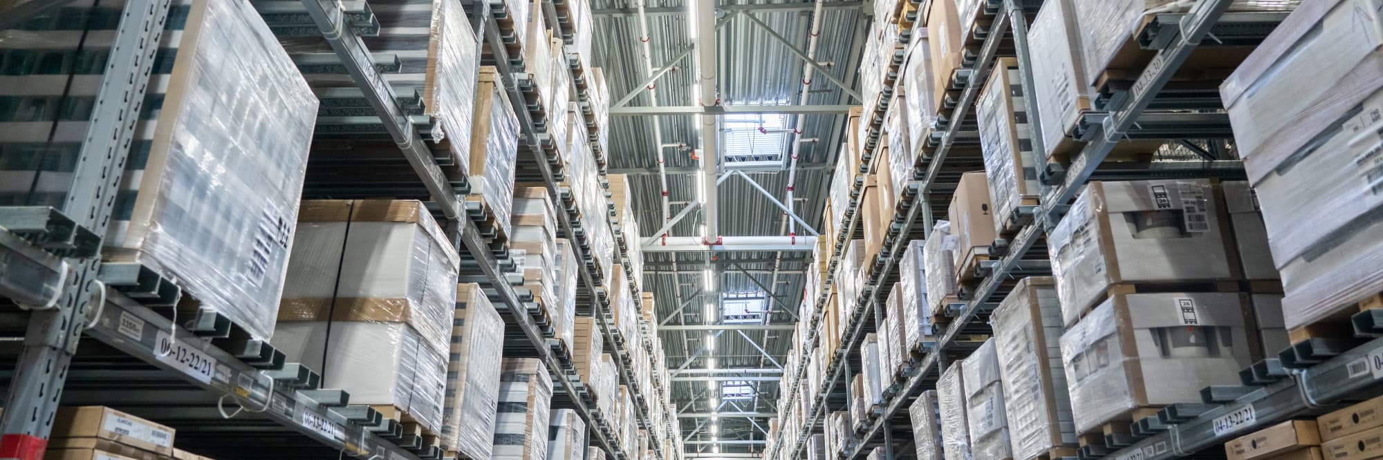 Warehouse aisle of stacked pallets under fluorescent light, the operational surface where forecast errors show up first