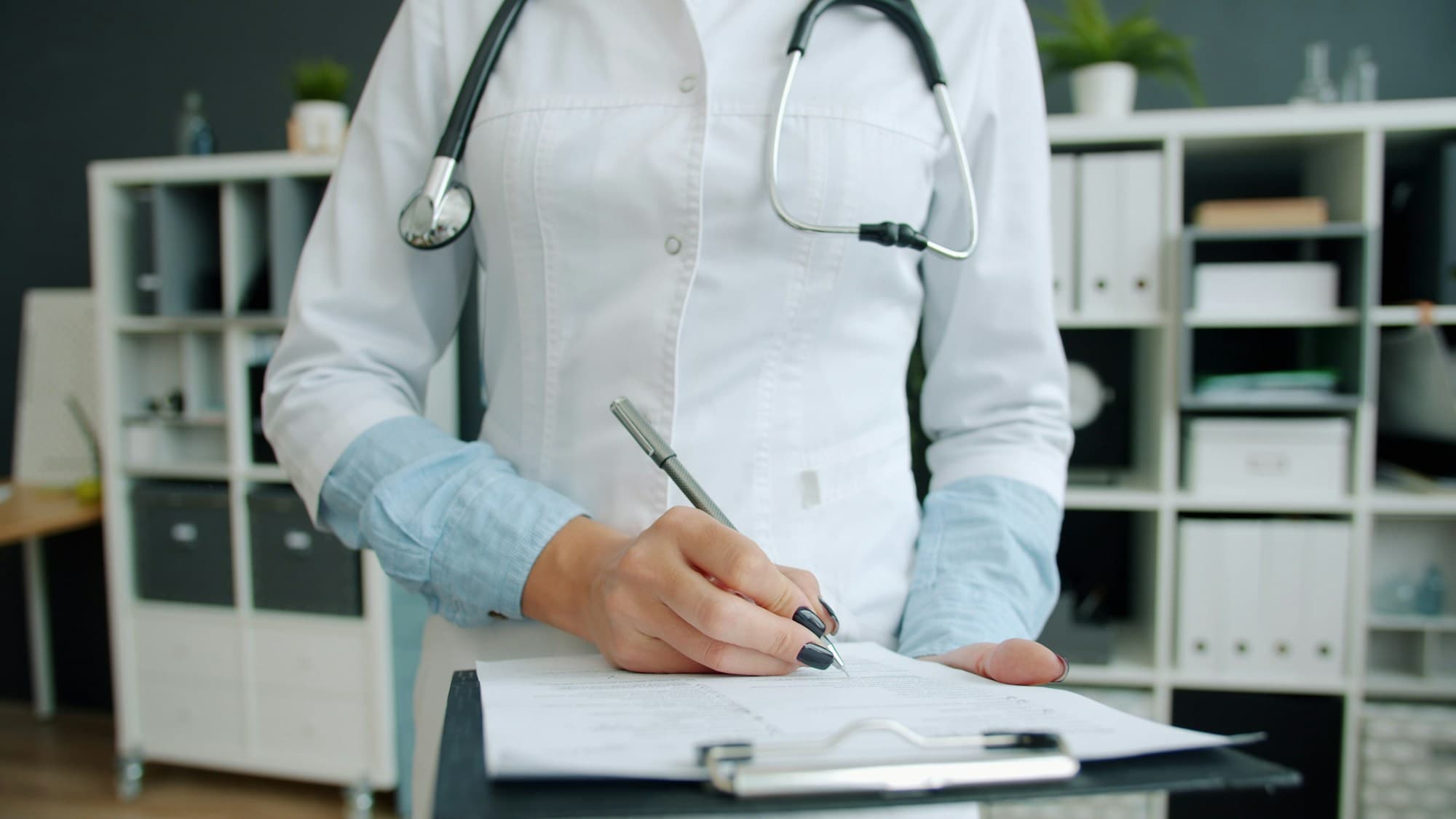 Clinician writing on a clipboard at a hospital desk, the operator-side documentation work that AI governance still depends on